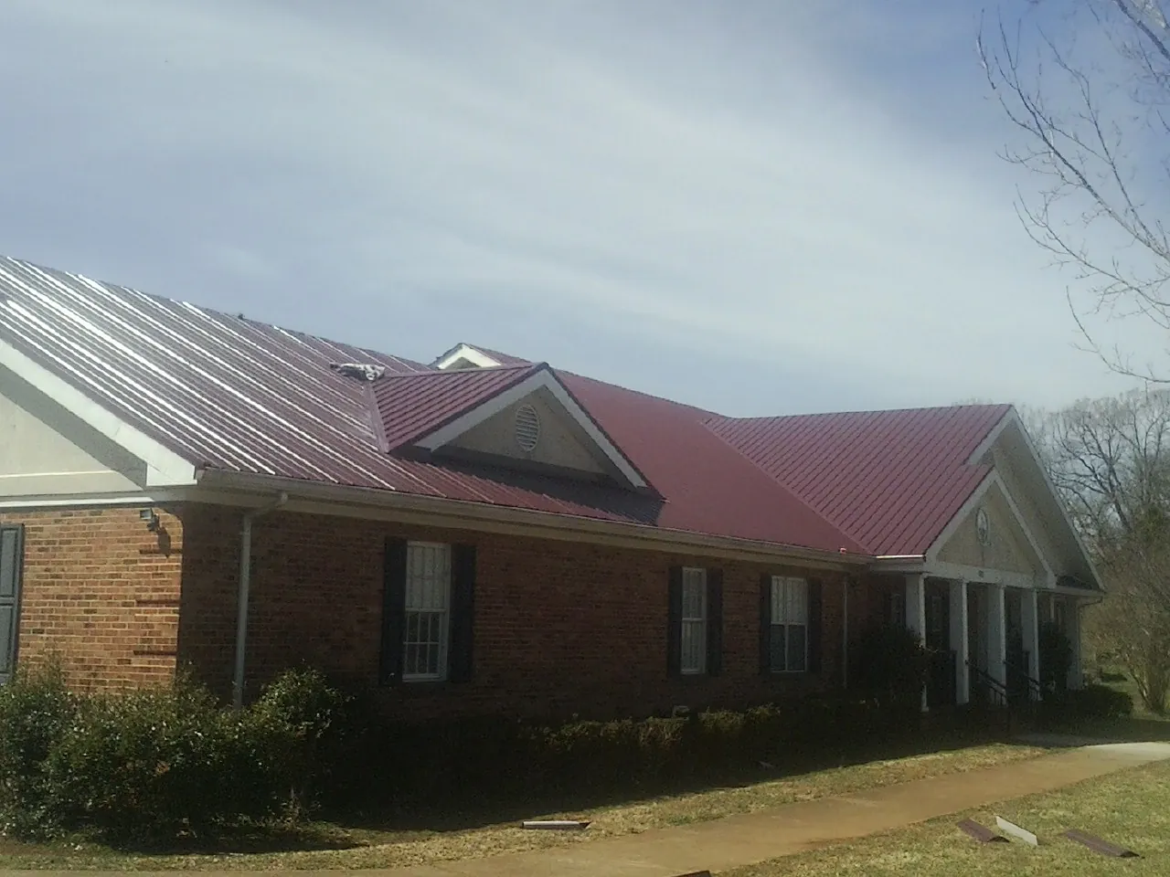 Red metal roof with gabled entries on a long brick building, from a Hail Damage Roof Repair job in Anthon