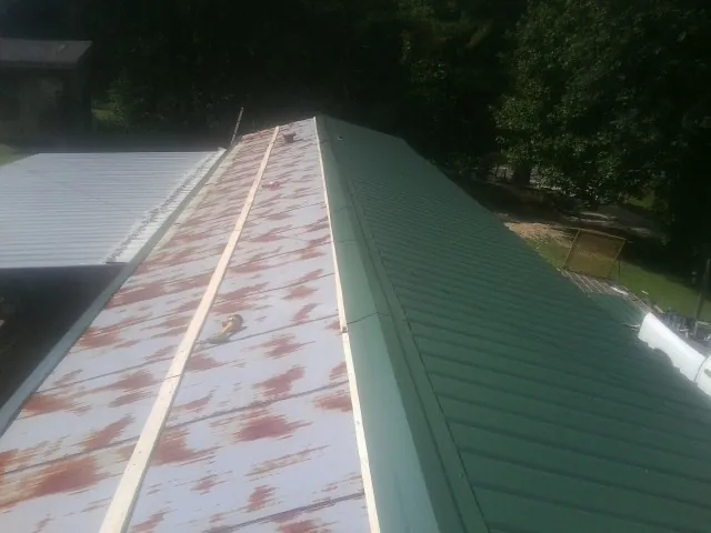 Old rusted panels beside newly installed green metal roofing — Wind Damage Roof Repair by Roofing Brothers in Anthon