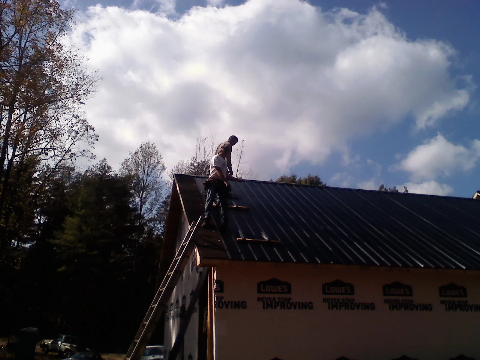 Roofer fastening dark metal panels high against a cloudy sky, from a Roof Inspection job in Anthon