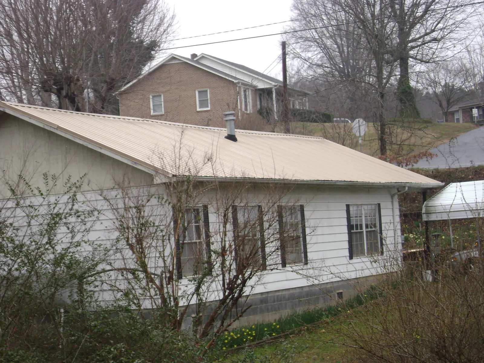 Tan metal roof on a white sided house set into a hillside — Commercial Roofing by Roofing Brothers in Anthon