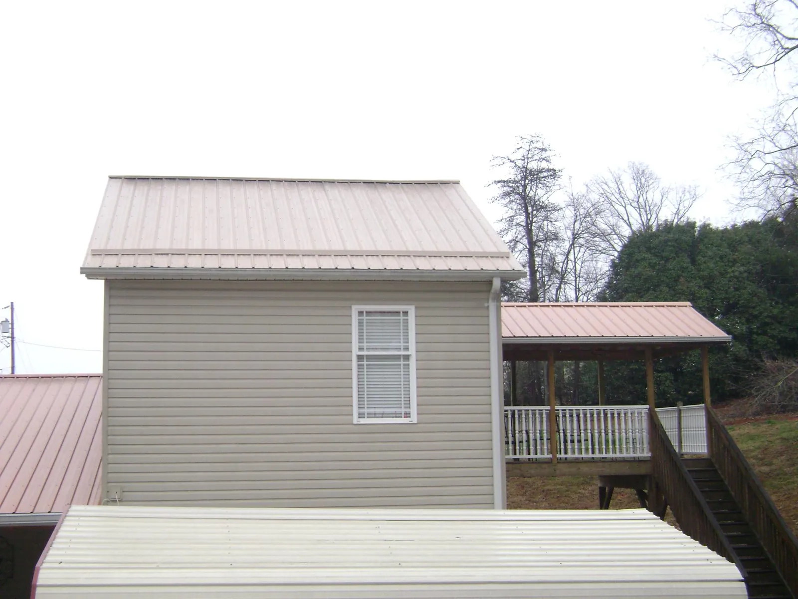 Tan metal roofs on a two story addition and attached porch, from a Roof Replacement job in Anthon